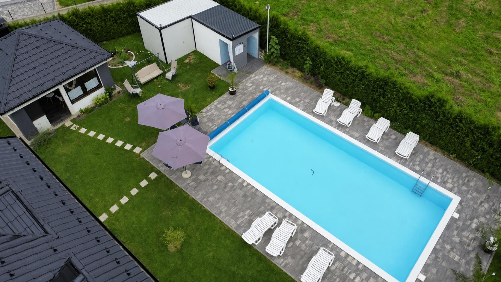 Povišen pogled na bazen, ležaljke, travnjak i natkriveni vrtni paviljon.
