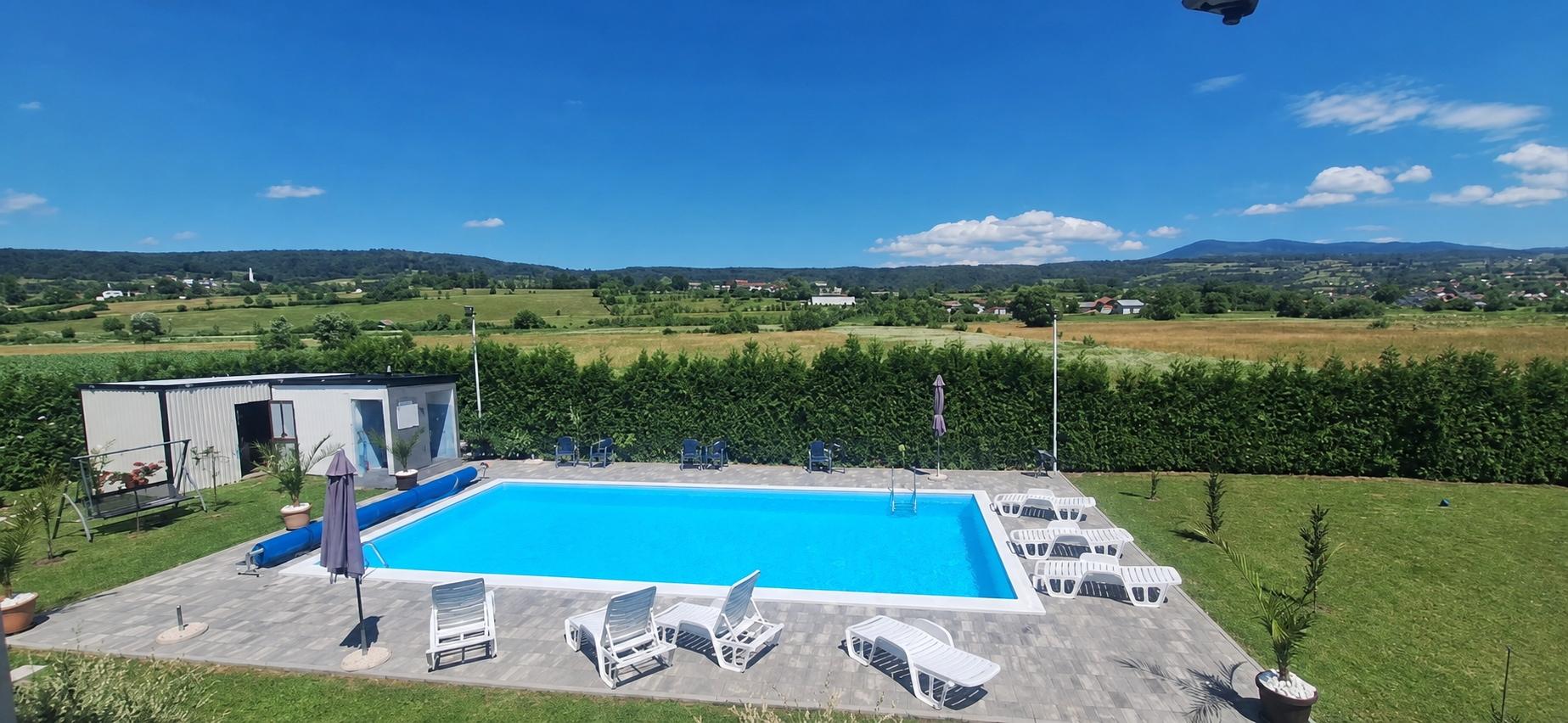 Širok pogled na vanjski bazen, travnjak i okolni krajolik.