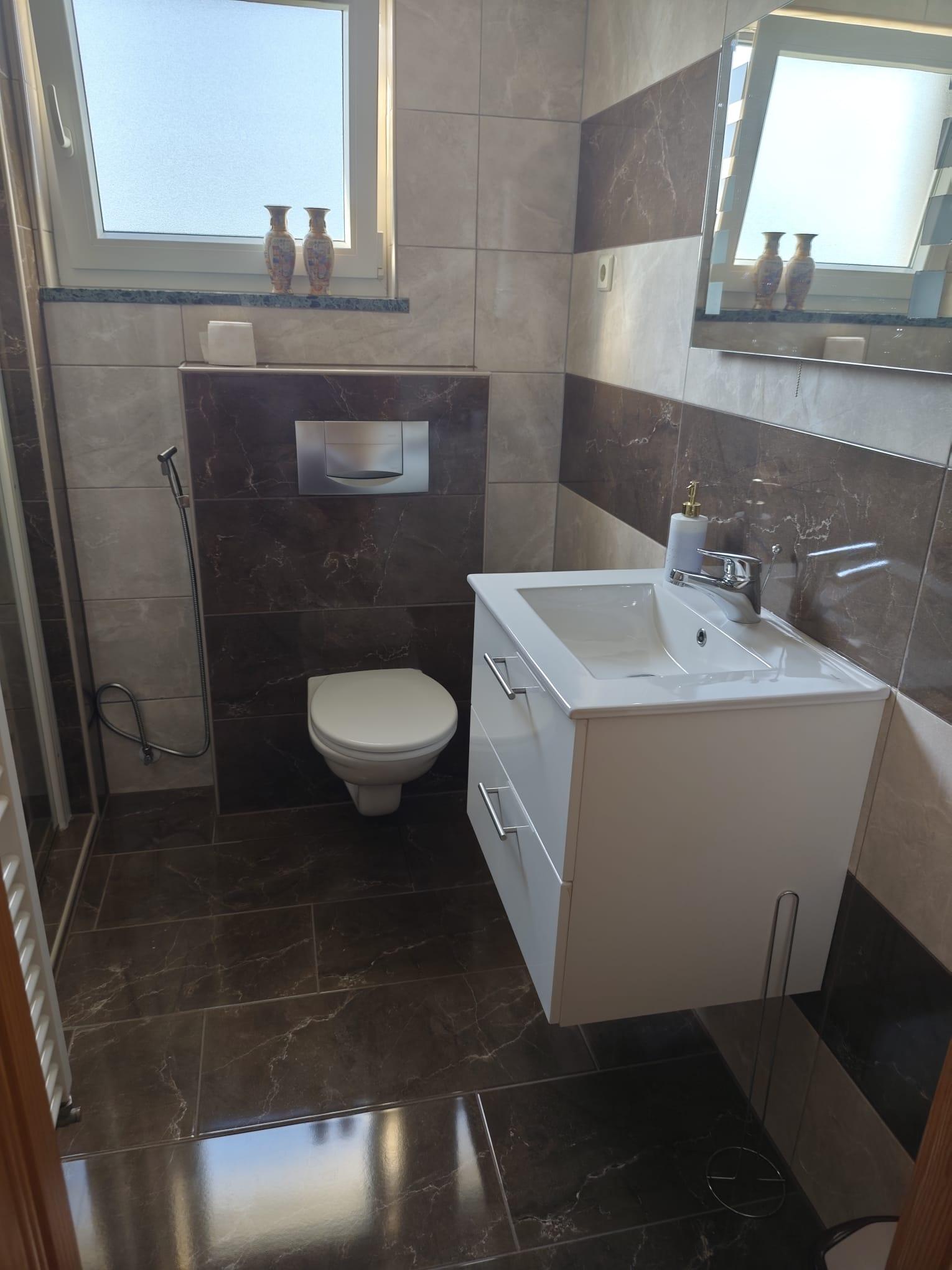 Kompaktes gefliestes Badezimmer mit wandmontierter Toilette, Waschtisch und Milchglasfenster.