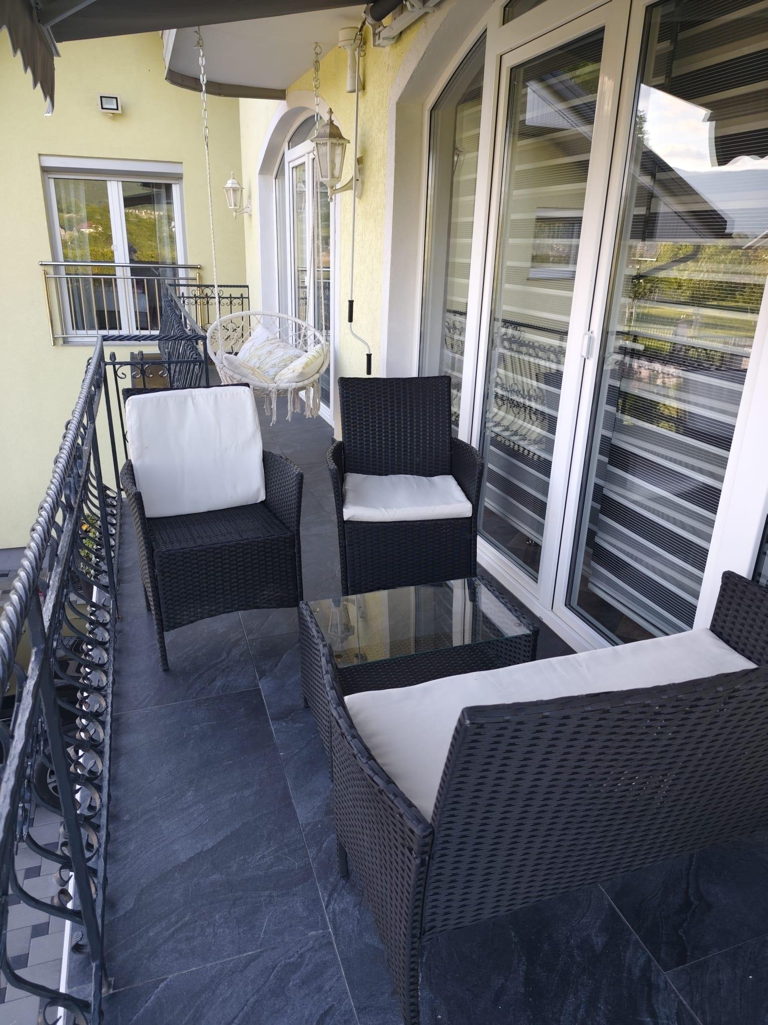 Sitzbereich auf dem Balkon mit Korbsesseln, einem Glastisch und einem Hängesessel.