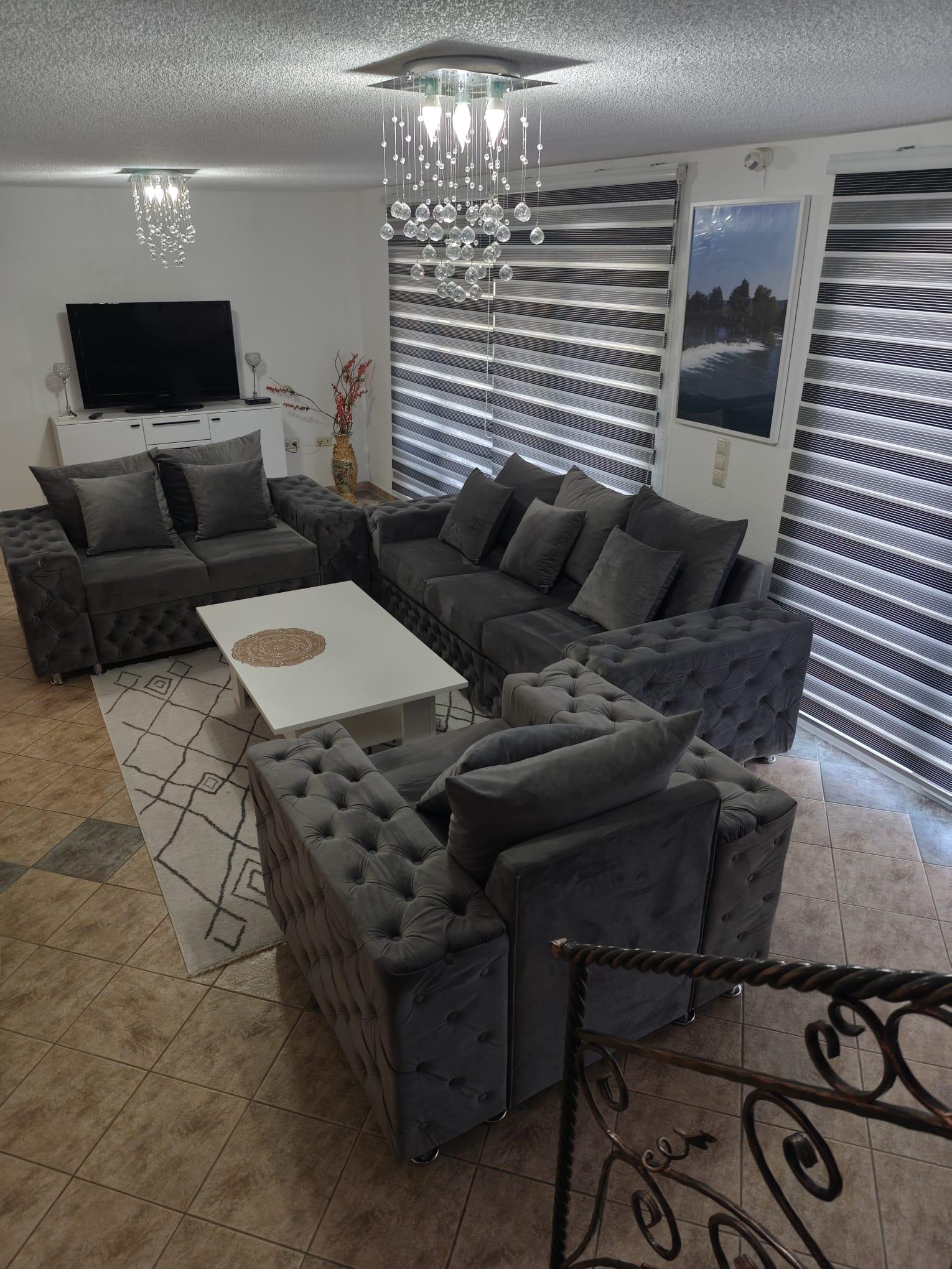 Wohnzimmer mit grauen Sofas mit Knopfheftung, einem weißen Couchtisch und einem Fernseher.